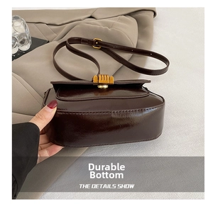 Detail view of the rounded bottom and stitching on a dark brown saddle bag with gold buckle