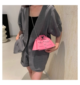 Detail of creative pink jacket-shaped mini bag with metal chain on a gray linen outfit