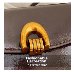 Macro shot of gold horseshoe buckle on brown oil wax leather minimalist saddle bag