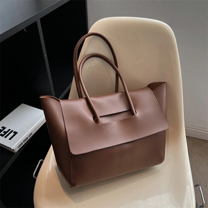 Brown leather tote bag with unique flap design on a chair in a modern room setting