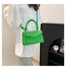 Detailed texture of a bright green woven crossbody bag with gold hardware and knotted handle