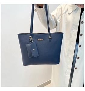 Macro detail of navy blue pebbled leather tote bag with gold logo and matching pouch