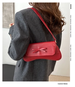 Red leather shoulder bag with a bow detail shown on a model in a tweed blazer