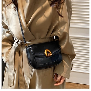 Close-up of black saddle bag with gold horseshoe buckle on a trench coat model