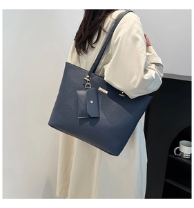 Detail view of navy tote bag with lychee texture and gold hardware on white trench coat