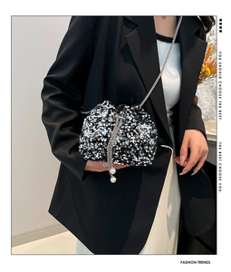 Detail of silver sequin bucket bag featuring pearl tassel and metal chain strap on model