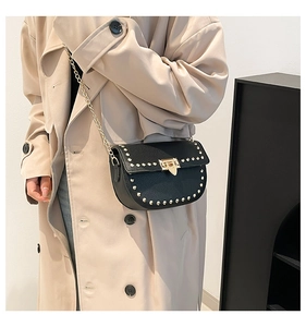 Close-up of black saddle bag with gold rivets and chain strap on a model shoulder