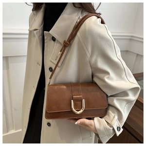 Dettaglio borsa a tracolla in pelle marrone con fibbia a U dorata su cappotto beige
