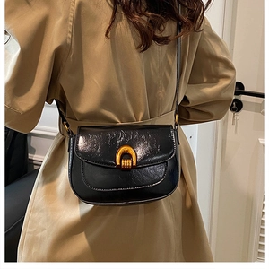 Detail of minimalist black saddle bag featuring glossy wrinkled leather and golden horseshoe buckle