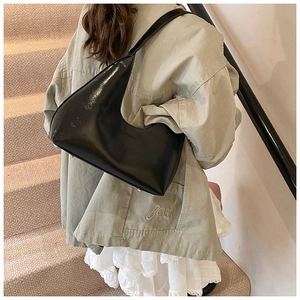 Close-up of a black glossy crescent shoulder bag with high-shine patent leather finish