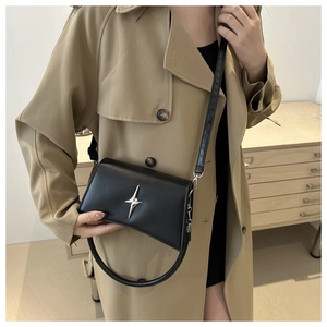 Dettaglio borsa a tracolla in pelle nera con stella d'argento su trench color kaki