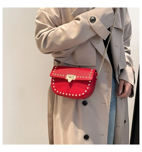 Détail du sac bandoulière rouge avec rivets dorés et chaîne sur un trench-coat