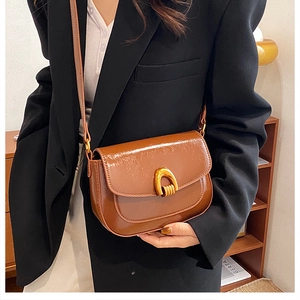 Detail of a brown leather saddle bag with a golden horseshoe buckle on a shoulder strap