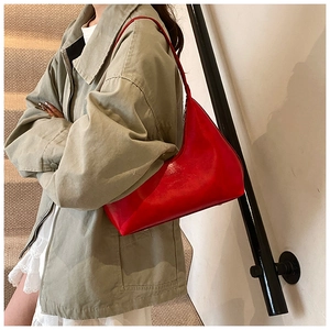 Side view of vibrant red glossy leather hobo crescent bag worn on a woman's shoulder