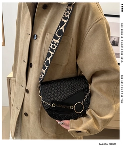 Détail du sac selle noir gaufré avec bandoulière géométrique large et détails chaîne dorée