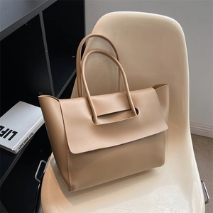 Minimalist beige oversized tote bag in smooth leather on an elegant white designer chair