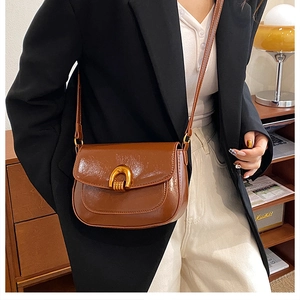 Close-up of vintage brown saddle bag with a decorative gold horseshoe buckle on a model
