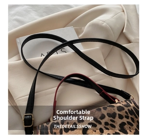 Detail view of leopard print bag featuring adjustable strap with red edge paint and gold buckle