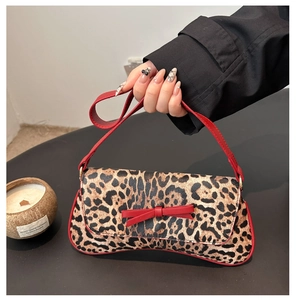 Detail of leopard print underarm bag featuring red bow accent and thin leather strap