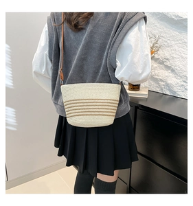 Detail of woven straw crossbody bag with brown stripes worn by model in minimalist setting
