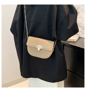 Close-up of beige lychee leather saddle bag with gold rivets and chain strap