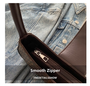 Close-up of smooth metal zipper and retro monogram texture on dark brown shoulder bag