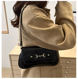 Detail of a black leather underarm bag featuring a metallic gold horsebit buckle accent