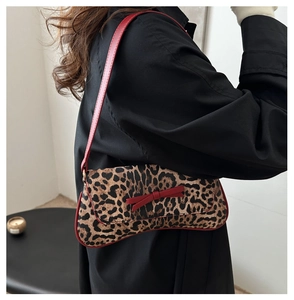 Detail of leopard print underarm bag with red bow and leather strap on model