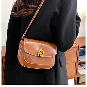 Detail of a brown leather saddle bag with a golden U-shaped buckle and crossbody strap