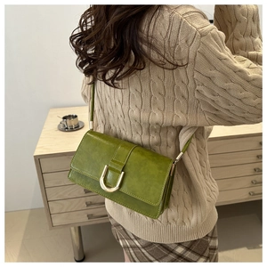 Dettaglio borsa baguette verde con fibbia a U dorata indossata su maglione beige