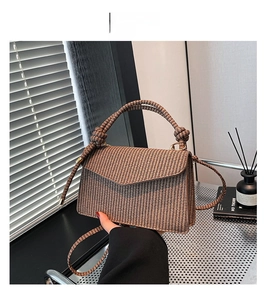 Detail of brown woven textured crossbody bag with unique knot handle in soft sunlight