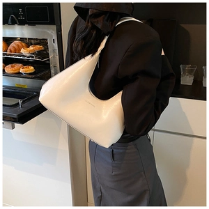 Close-up of a minimalist white leather hobo bag worn by a model in a modern cafe setting