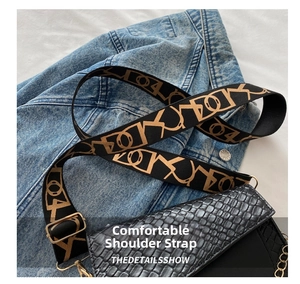Détail du sac selle noir texturé avec sa large bandoulière en jacquard et boucle dorée