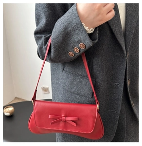 Detail of red baguette shoulder bag with chic bow accent on a wool blazer background