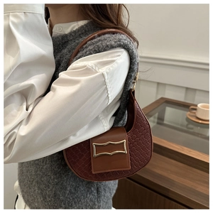 Dettaglio di borsa a spalla marrone intrecciata con fibbia dorata su camicia bianca