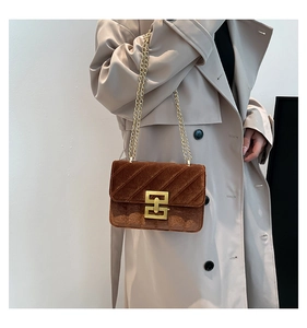 Sac bandoulière en velours marron avec chaîne dorée et fermoir sur un mannequin en trench