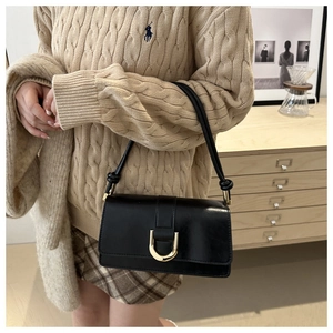 Dettaglio borsa baguette in pelle nera con fibbia a D dorata indossata da modella