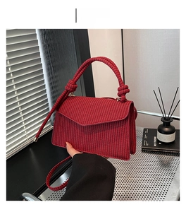 Detail of red woven handbag with envelope flap and knotted circular handle on a desk
