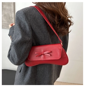 Side view of a red small square bag with bow detail on a grey blazer outfit