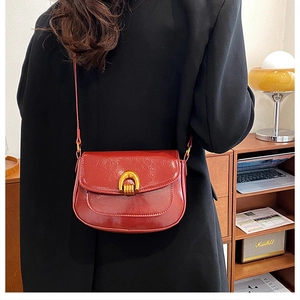 Detail view of burgundy saddle bag with glossy patent leather and golden buckle
