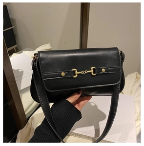 Detail of a black leather shoulder bag featuring a gold horse-bit metal buckle closure