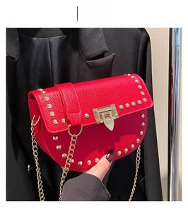 Détail du sac selle rouge en cuir grainé avec rivets dorés et bandoulière chaîne