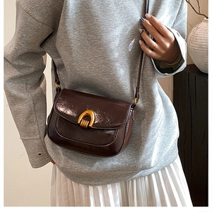 Detail of dark brown saddle bag with golden horseshoe buckle worn with a casual outfit