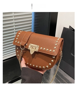 Détail latéral du sac en cuir grainé marron avec rivets dorés et bandoulière chaîne