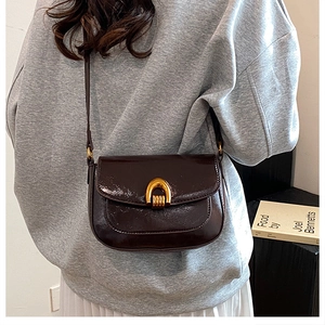 Detail of dark brown patent leather saddle bag with gold horseshoe buckle closure