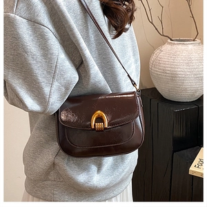 Detail of dark brown saddle bag with golden U-shaped buckle on a minimalist backdrop