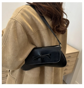 Detail of black PU leather shoulder bag with a bow accent and gold hardware strap