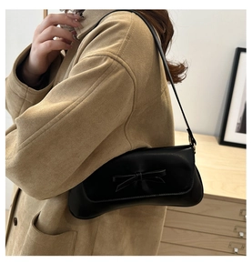 Close-up of minimalist black bow shoulder bag styled with a casual trench coat