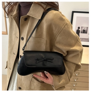 Close-up of black leather underarm bag featuring a delicate bow and curved base