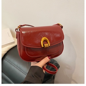 Detail of red glossy leather saddle bag featuring a distinctive gold U-shaped metal lock
